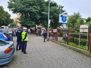 policjant i policjantka ruchu drogowego stoją przed bramą wejściową na teren Szkoły Podstawowej nr 1 w Mysłowicach