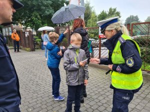 policjantka wręcza element odblaskowy chłopcu przed szkołą