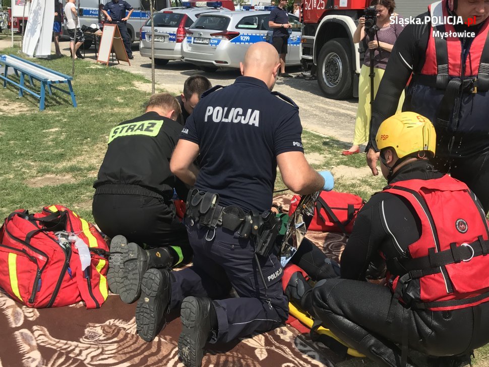 Zdjęcie archiwalne z 2018r. Policjant i strażacy udzielają pierwszej pomocy osobie wyciągniętej z wody.