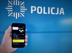 smartfon trzymany w ręku na tle loga &quot;POLICJA&quot;