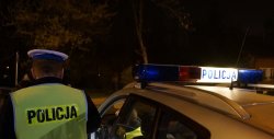 Na zdjęciu widoczny policjant przy radiowozie z kamizelką odblaskową z napisem POLICJA na plecach