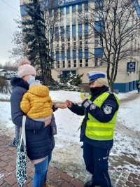 policjantka wręcza elementy odblaskowe kobiecie z małym dzieckiem na ręce