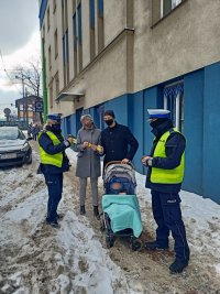 policjanci wręczają elementy odblaskowe trzyosobowej rodzinie