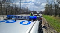 na pierwszym planie policyjny radiowóz, w tle dwóch policjantów przeprowadzających kontrolę drogową