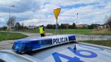 na pierwszym planie policyjny radiowóz, w tle policjant obserwujący ruch pojazdów