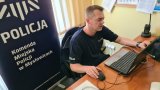 policjant siedzący przy laptopie podczas spotkania w formie online z uczniami. W tle rollup Komendy Miejskiej Policji w Mysłowicach