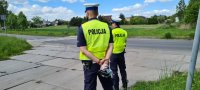 dwaj policjanci obserwujący ruch pojazdów. Jeden z policjantów trzyma w rękach za plecami reklamówkę ze słodyczami