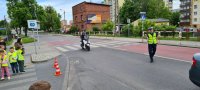 policjant zatrzymuje do kontroli kierowcę motoroweru. Na chodniku stoją dzieci.