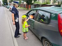 dziewczynka wręcza kierowcy laurkę przez szybę pojazdu. Przy niej stoi policjantka ruchu drogowego.
