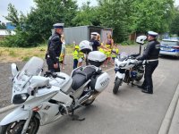 Na pierwszym planie policyjne motocykle i policjanci w umundurowaniu na motocykl. W tle przedszkolaki z policjantką i opiekunkami.