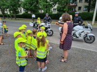 Przedszkolaki w żółtych kamizelkach i czapkach przy policyjnych motocyklach. Na jednym z motocykli siedzi dziewczynka, a przy niej stoi policjant