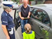 policjantka i dziewczynka wręczają kierowcy laurkę z okazji Dnia Ojca