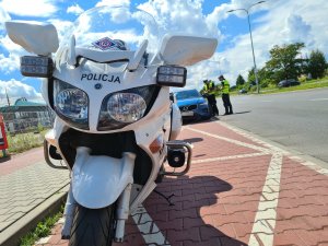 na pierwszym planie policyjny motocykl, w tle policjanci ruchu drogowego w trakcie kontroli volvo