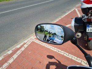 W odbiciu lusterka policyjnego motocykla widać policjantów kontrolujących kierowcę volvo.