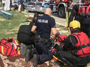 Zdjęcie archiwalne z pokazów ratownictwa wodnego w 2018. Na zdjęciu policjant oraz strażacy udzielają pierwszej pomocy osobie wyciągniętej z wody.