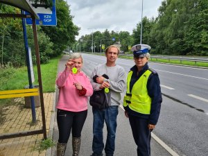 policjantka ruchu drogowe wraz z kobietą i mężczyzną, którzy trzymają w ręku elementy odblaskowe