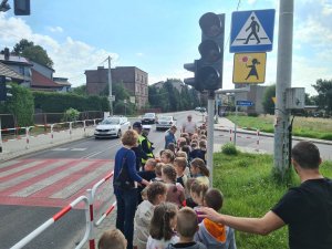 policjantka ruchu drogowego i policjant tłumaczą dzieciom zasady bezpieczeństwa przy przejściu dla pieszych