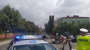 policjant ruchu drogowego przy radiowozie zabezpieczający przejazd parady motocyklowej