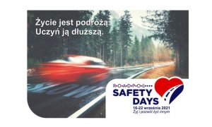 Droga prowadząca łukiem  przez zalesiony teren. Po drodze pędzi czerwony samochód, którego sylwetka jest zamazana. Napis białą czcionką: Życie jest podróżą. Uczyń ją dłuższą.  W prawym dolnym rogu napis: ROADPOL Safety Days 16-22 września 2021. Żyj i pozwól żyć innym. Obok rysunek serca, w które wkomponowana jest droga.