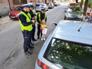 troje policjantów ruchu drogowego i dziewczynka z przedszkola wręczają kierowcy mandat przygotowany przez przedszkolaków