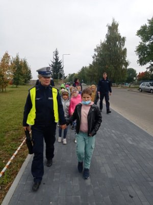 policjantka i policjant idący chodnikiem z grupą uczniów