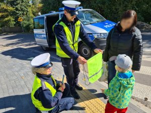 policjant ruchu drogowego wręcza chłopcu odblaskowy worek na buty