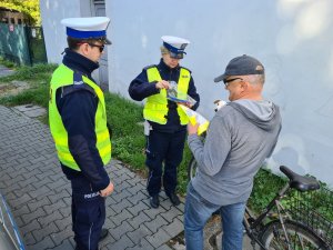 policjanci ruchu drogowego wręczają rowerzyście kamizelkę odblaskową i opaskę