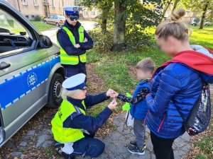 policjantka ruchu drogowego wręcza chłopcu i jego mamie elementy odblaskowe