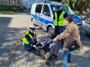 policjantka ruchu drogowego wręcza elementy odblaskowe dziecku w wózku