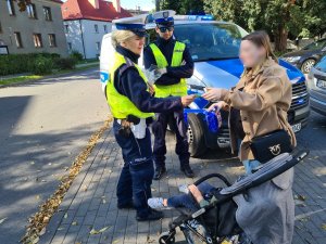 policjanci ruchu drogowego wręczają elementy odblaskowe mamie prowadzącej wózek dziecięcy