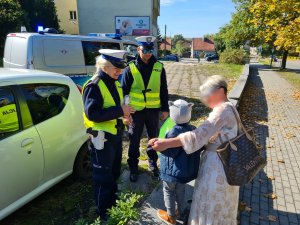 policjanci ruchu drogowego wręczają elementy odblaskowe dziecku i jego babci