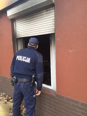 Policjant zagląda do wnętrza budynku przez okno