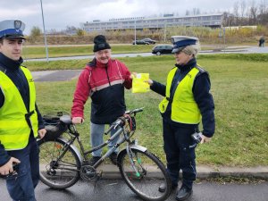 policjanci wręczają rowerzyście kamizelkę odblaskową