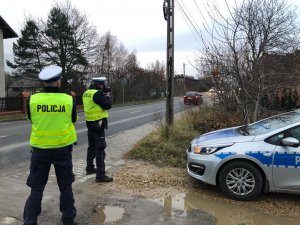 policjanci ruchu drogowego mierzący prędkość. Po prawej stronie radiowóz policyjny.