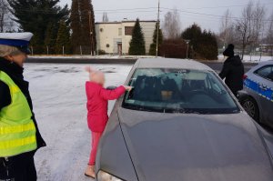 policjantka obserwująca kobietę z dzieckiem odśnieżającą pojazd