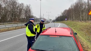 policjanci stojący przy czerwonym pojeździe który kontrolują