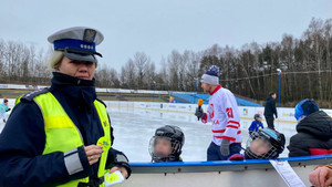 policjantka prezentująca element odblaskowy. w tle odbywa się trening hokeja na lodowisku