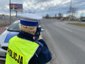 policjantka dokonująca pomiaru prędkości, w tle radiowóz