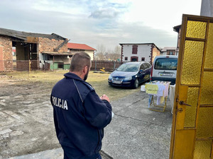 policjant stojący przed domem, w tle samochody