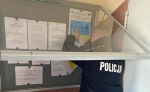 policjant umieszczający plakaty informacyjne