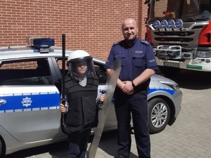policjant pozujący do zdjęcia z dzieckiem, które ma na sobie policyjny strój ochronny oraz chełm
