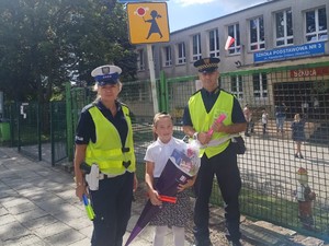 policjantka wraz ze strażnikiem miejskim rozdający elementy odblaskowe dzieciom