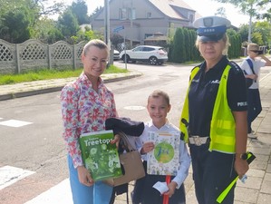 policjantka wraz ze strażnikiem miejskim rozdający elementy odblaskowe dzieciom