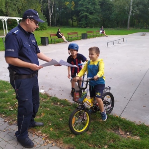 zdjęcie przedstawia policjanta rozdającego ulotki dzieciom