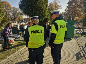 zdjęcie przedstawia policjantów na cmentarzu rozdających elementy odblaskowe.