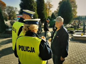 zdjęcie przedstawia policjantów na cmentarzu rozdających elementy odblaskowe.