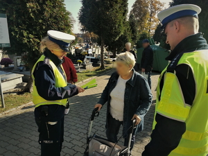 zdjęcie przedstawia policjantów na cmentarzu rozdających elementy odblaskowe.