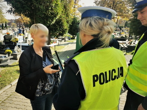 zdjęcie przedstawia policjantów na cmentarzu rozdających elementy odblaskowe.