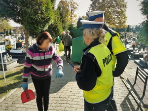 zdjęcie przedstawia policjantów na cmentarzu rozdających elementy odblaskowe.