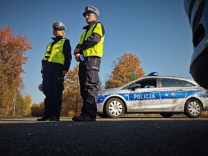 Zdjęcie przedstawia policjantów stojących przy radiowozie obserwujących ruch pojazdów